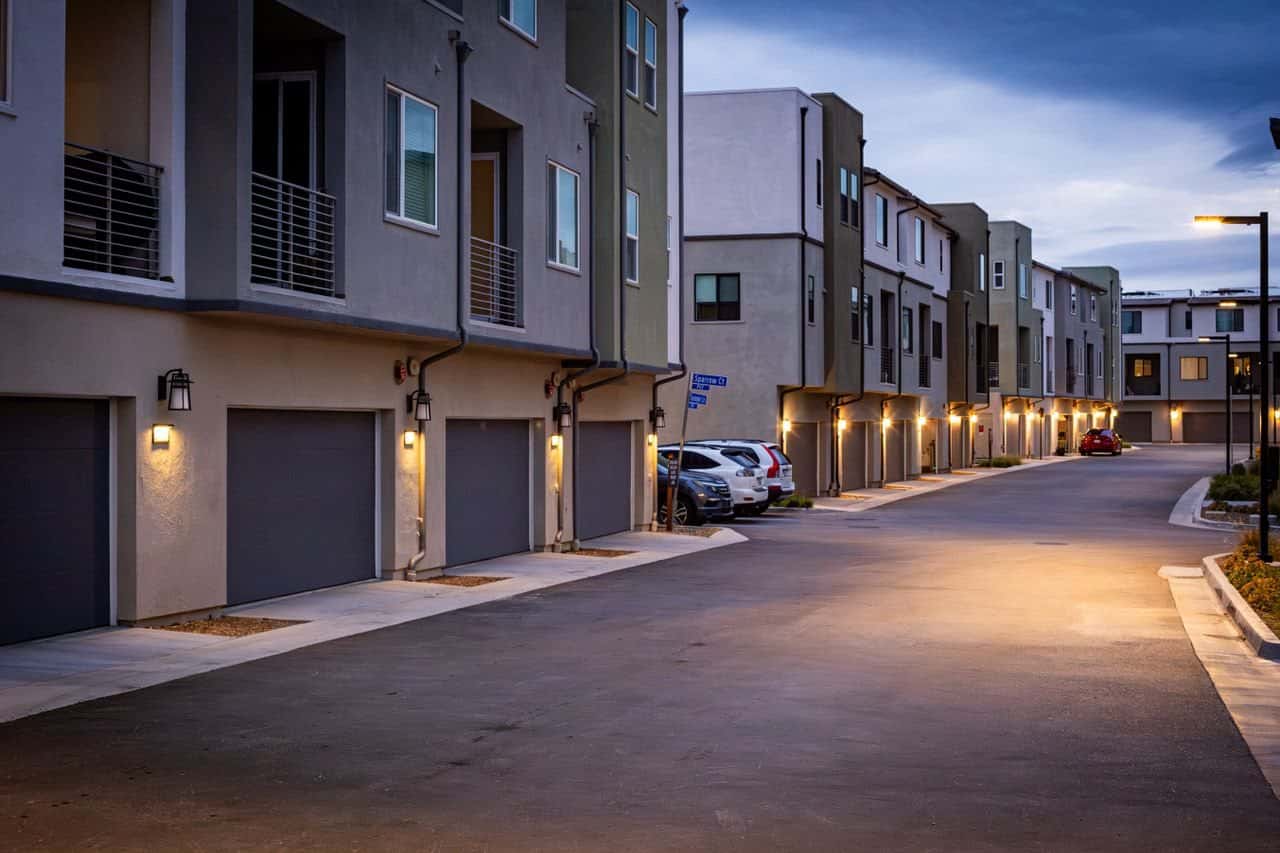 A quiet street of townhomes at dusk, garage lights on.